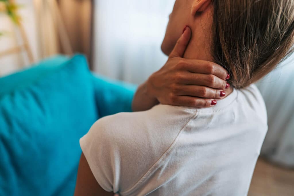 Woman suffering from neck pain at home, holding her hand on the cervical area